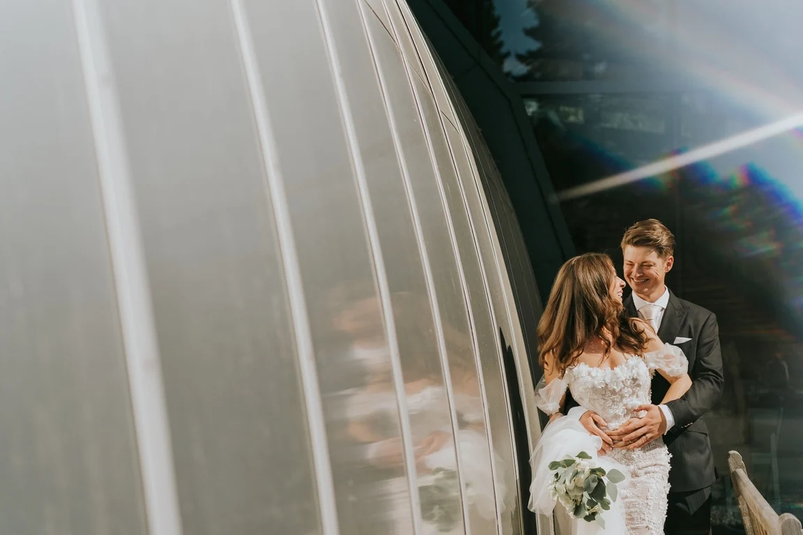 Bride and groom beside a curved glass wall