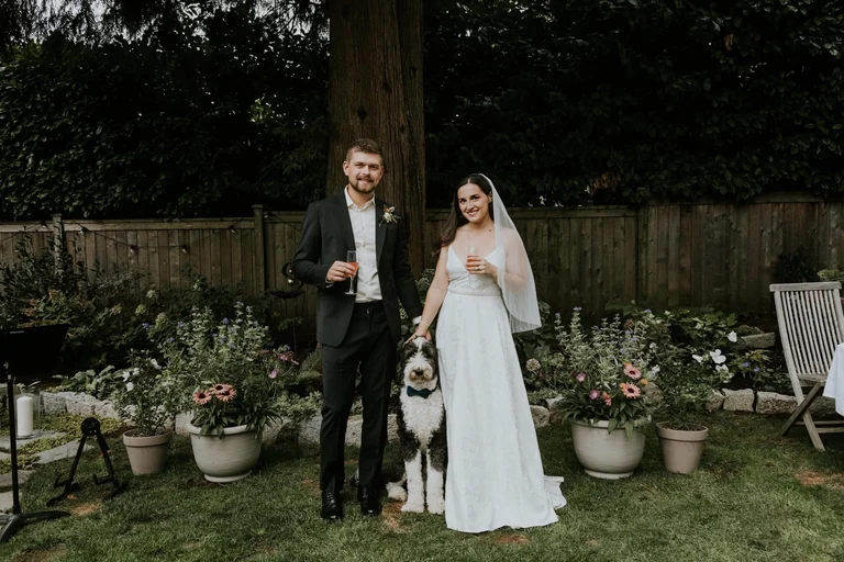 Bride and groom posing beside a garden fence