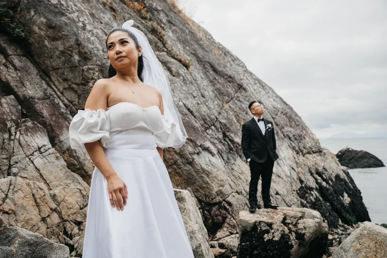 Bride and groom posing beside a rocky shoreline