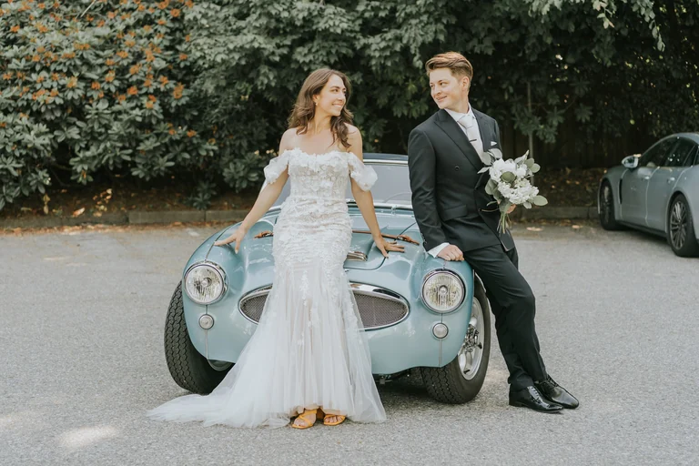 Bride and groom posing beside a vintage car