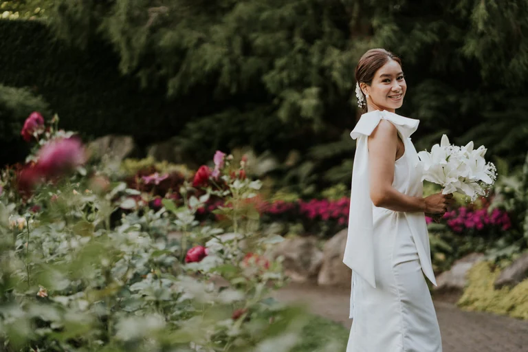 Bride holding a bouquet beside flowering shrubs