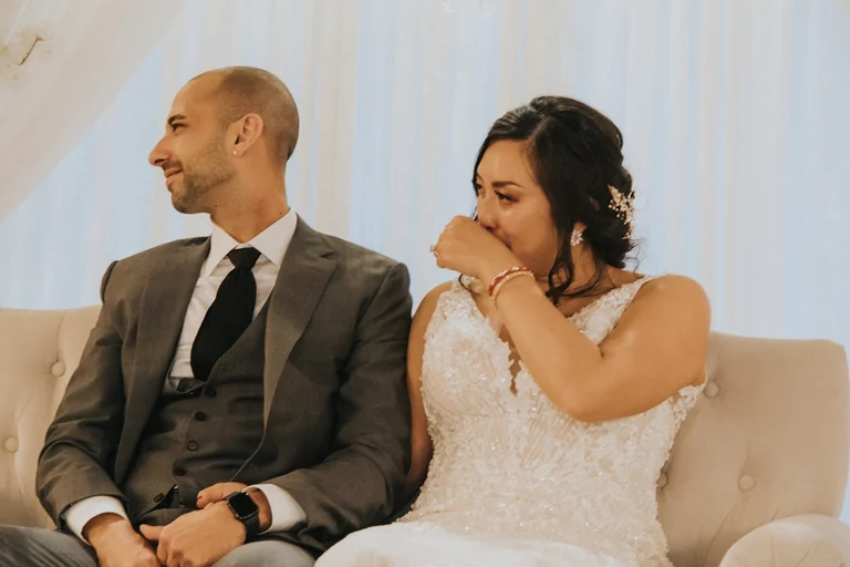 Bride wiping a tear while seated beside the groom