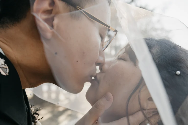 Close-up of newlyweds kissing beneath a veil