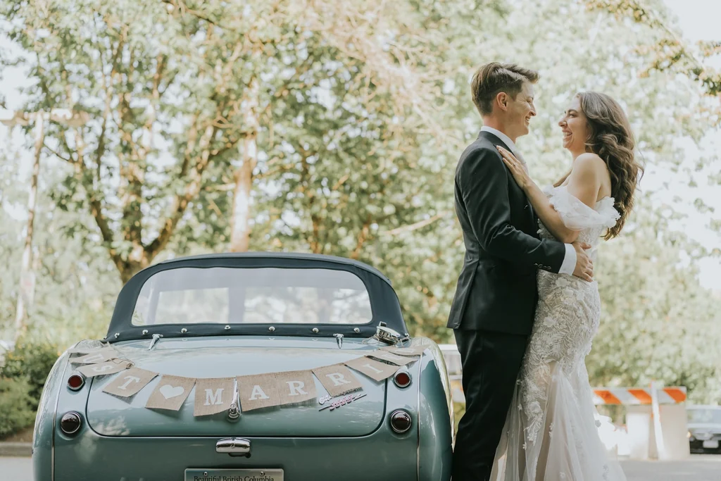 Newlyweds beside a decorated vintage convertible