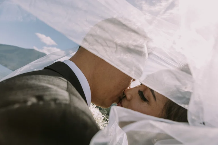 Newlyweds kissing beneath a flowing veil