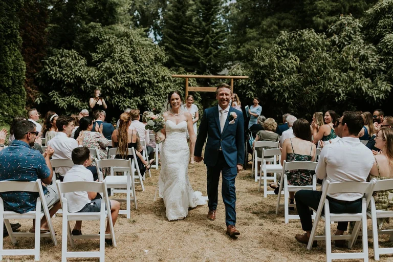 Newlyweds walking down an outdoor ceremony aisle