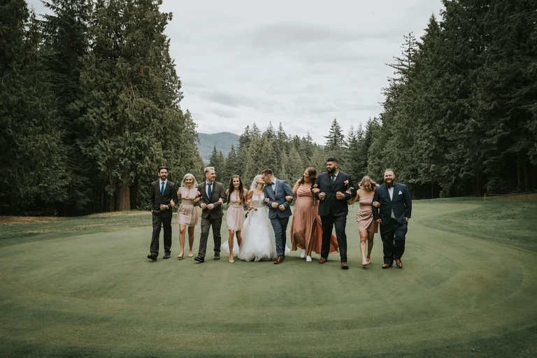 Wedding party posing on a lawn surrounded by trees