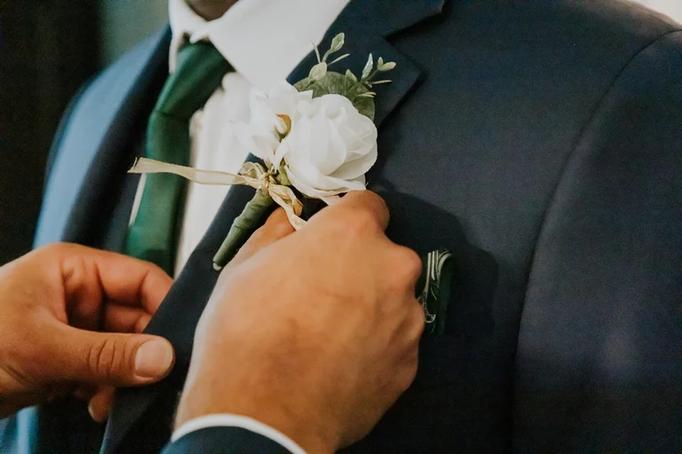 White boutonniere being pinned to a wedding suit